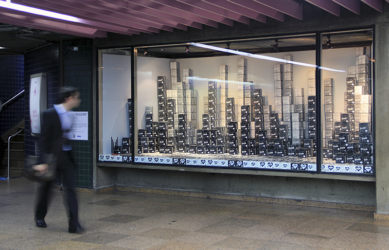 Amor e Prestígio, 2013-2014

embalagens de papel fotocopiadas em preto e branco

dimensões variadas

[Projeto Vitrinas - MASP, estação de metrô Trianon-MASP, São Paulo, SP.

Instalado na vitrine da estação de metrô, composto com dois elementos constituidores da paisagem urbana: uma calçada, cujo desenho forma o logo do mapa do Estado de São Paulo junto a um conglomerado de arranha-céus. A composição dos prédios foi feita com as embalagens do chocolate Prestígio e a calçada foi construída com embalagens da paçoca Amor.]
