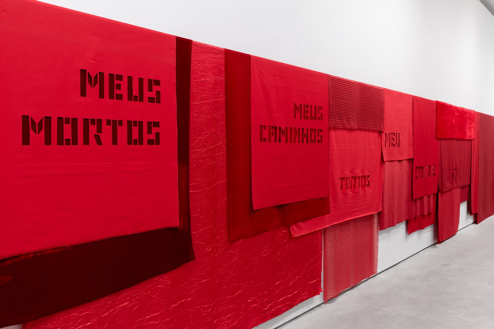 	VEIAS ABERTAS, 2024

	tecidos vermelhos recortados com frases da musica Sangue Latino

	150 x 1800 cm